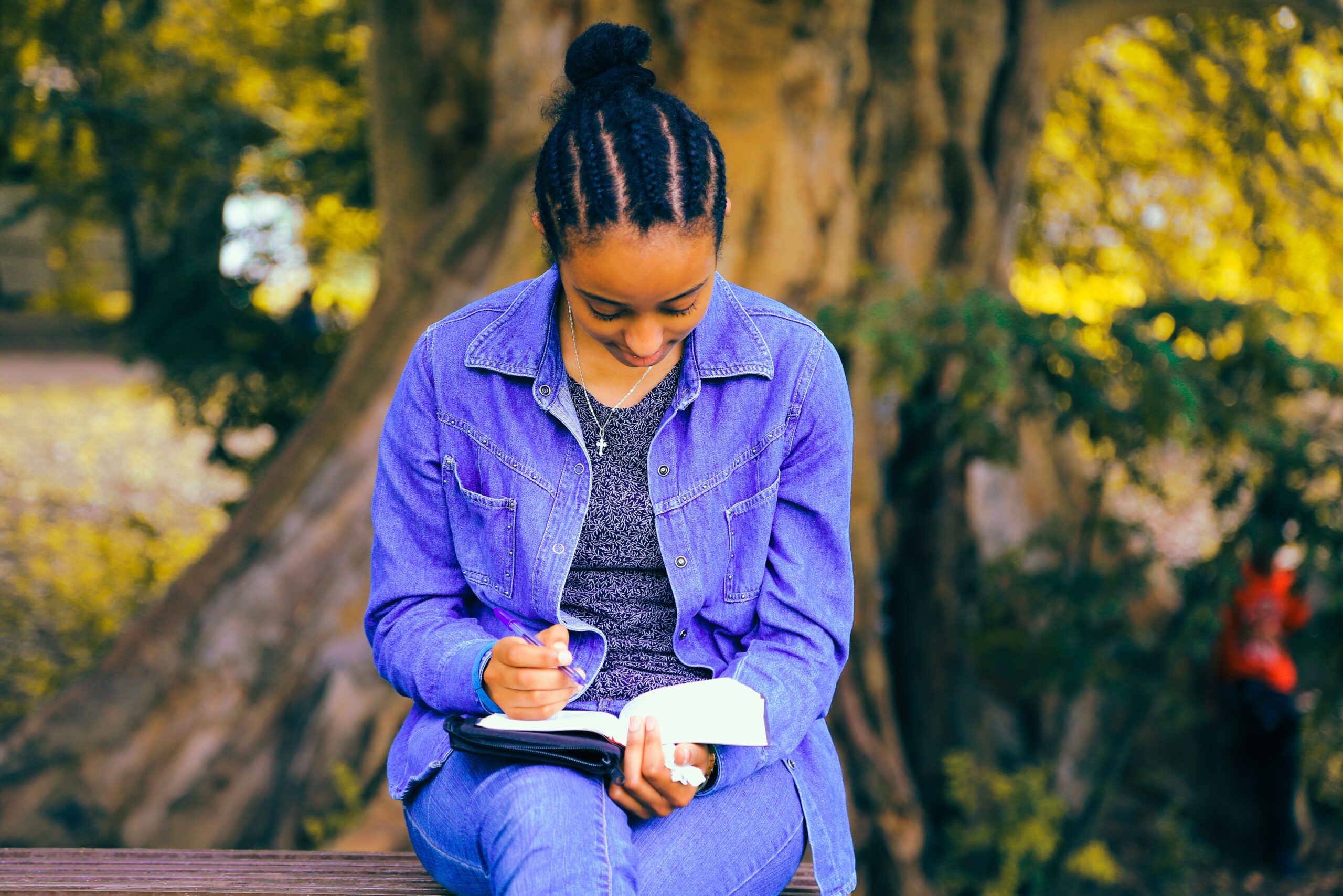 Girl sitting on a bench in a park journaling