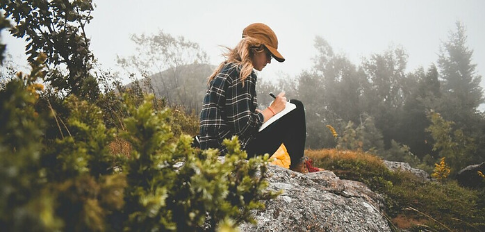 Girl sitting on a rock journaling