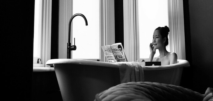 A black and white image of a lady sitting in a tub reading a book