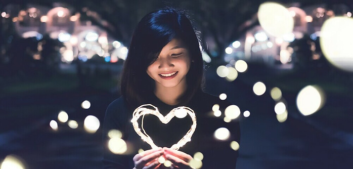 Girl holding a heart shaed glowing object and smiling to it