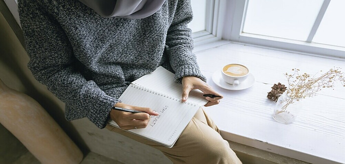 girl sitting by the window with a cup of coffee and a journal 