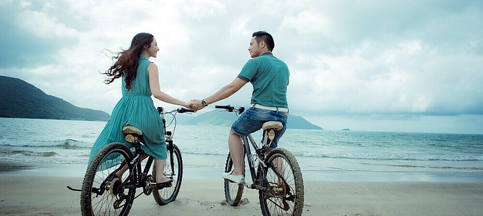 man and woman on their bicycles holding hands at the beach